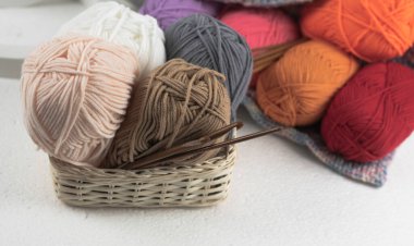 İplik topları ve ahşap örgü kancaları örülmüş sepet, bulanık aydınlatma.