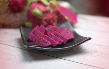 Kırmızı Ejder meyvesi dilimlenmiş, siyah tabağa konmuş, bulanık ışık yayılmış.