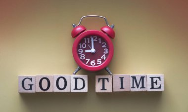 Kırmızı alarmlı saat, ahşap blok ve sanat tonu üzerine yazılmış Good TIME sözcüğünü takar.