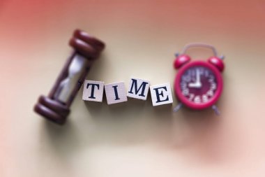 Bulanık kum saati ve kırmızı alarm saatinin ortasına koyulan ahşap bloğa yazılmış TIME sözcüğünün seçici odak noktasında, bulanık ışık