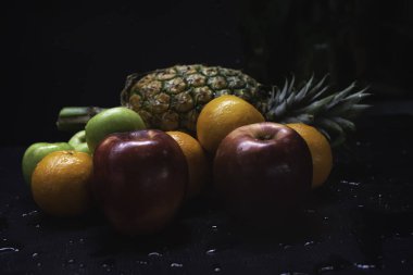 Karışık meyveler. Arka planda ananas, elma ve portakal var. Su damlasıyla ıslanmış.