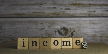 Tahta bloğa yazılmış INCome kelimesi kereste tahtasına konmuş, bulanık ışık etrafında