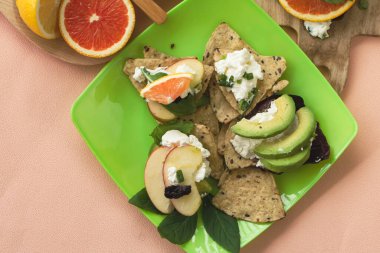 Dilimlenmiş portakal, avokado, elma, krem peynir ve çoklu tahıllı ekmek, ev yapımı aperatif. Meyve kanalı, pastel arka plan.