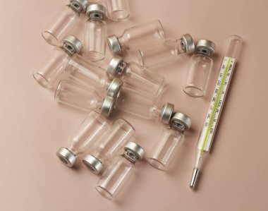 Aşı cam şişesi ve klinik termometre pastel arka plana yerleştirildi.