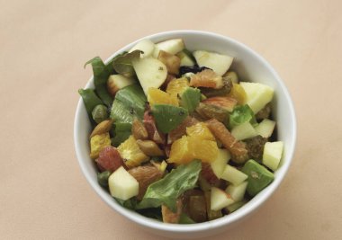 Beyaz seramik kaseye karıştırılmış meyve salatası, pastel arka plan.