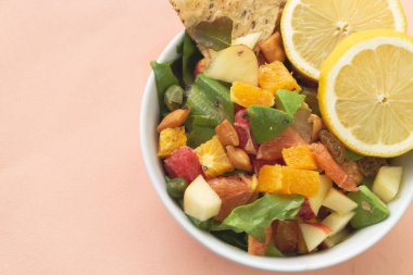 Beyaz seramik kasede dilimlenmiş limonla karıştırılmış meyve salatası, pastel arka plan.