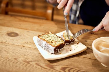 Bir kadının ellerinin bir dilim limon ve haşhaşlı kek kesmesi, bir fincan kahveyi ahşap bir masada kesmesi. Boşluğu kopyala.