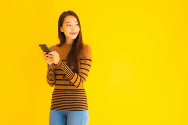 Güzel genç Asyalı kadın, sarı izole edilmiş arka planda birçok eylem içeren akıllı cep telefonu ya da cep telefonu kullanır.
