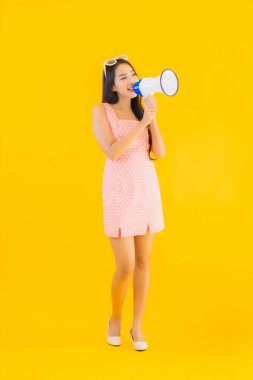 Güzel bir Asyalı kadın, sarı izole edilmiş arka planda megafonla yüksek sesle konuşur.