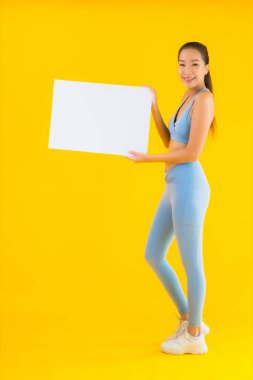 Güzel bir Asyalı kadın portresi spor giysisi giyer. Sarı izole edilmiş arka planda boş beyaz ilan panosu var.
