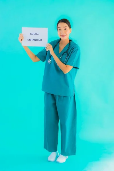 Portrait beautiful young asian doctor woman show sign with Social distancing on blue isolated background