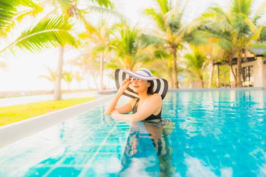 Güzel bir Asyalı kadın portresi, gün batımında palmiye ağacıyla birlikte havuz kenarında dinleniyor ya da tatil için gün doğumunda dinleniyor.