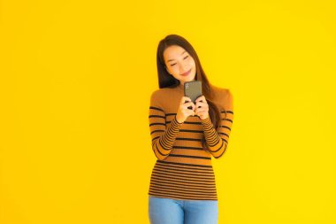 Güzel genç Asyalı kadın, sarı izole edilmiş arka planda birçok eylem içeren akıllı cep telefonu ya da cep telefonu kullanır.