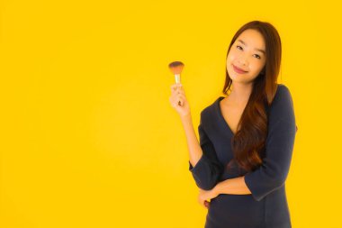 Sarı izole arkaplanda makyaj fırçası olan güzel bir Asyalı kadın portresi.