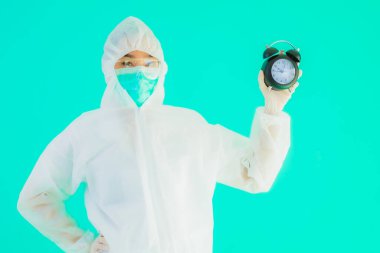 Güzel bir portre genç Asyalı doktor. Özel süit ve maske takıyor. Mavi arka planda saati ya da alarmı gösteriyor.