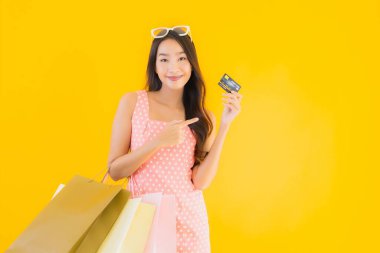 Renkli alışveriş çantalı güzel Asyalı kadın akıllı cep telefonu ve sarı izole edilmiş arka planda kredi kartı.