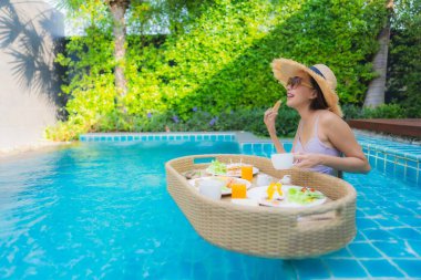 Genç Asyalı kadının portresi mutlu bir gülümseme ile otel havuzunda yüzen kahvaltı tepsisinin keyfini çıkar.