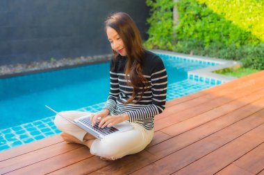 Genç Asyalı bir kadının portresi oteldeki yüzme havuzunda dizüstü bilgisayar kullanıyor.