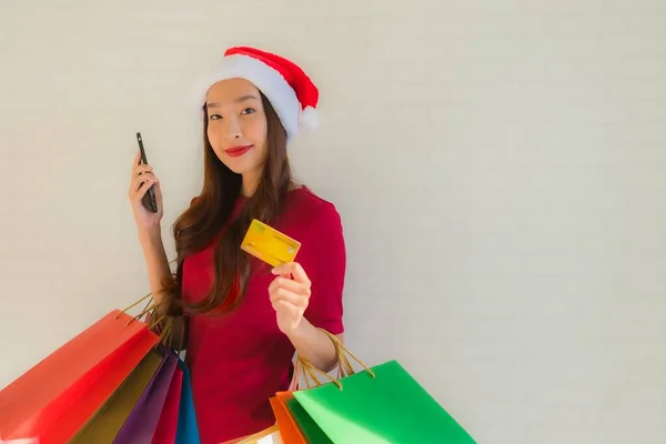 肖像画の美しい若いアジアの女性は ショッピングバッグスマート携帯電話とクレジットカードでクリスマスサンタの帽子を着用 — ストック写真