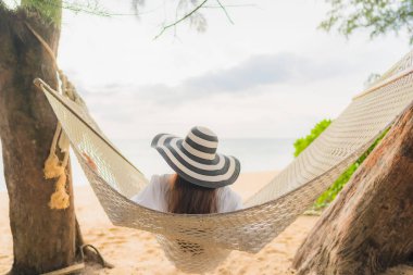 Güzel bir Asyalı kadın portresi deniz kıyısındaki hamakta dinleniyor.