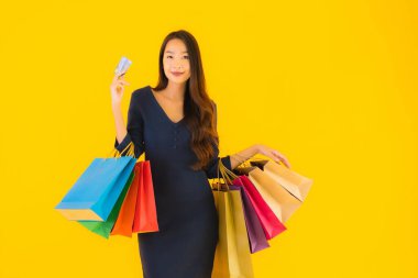 Portre güzel genç Asyalı kadın alışveriş çantası kredi kartı ve akıllı cep telefonu sarısı izole bir arka plan.