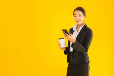 Portre güzel genç Asyalı kadın akıllı cep telefonu ve kahve fincanı ile izole edilmiş sarı arka planda