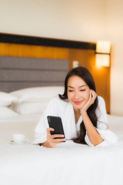Güzel bir Asyalı kadın yatak odasının içinde akıllı cep telefonu kullanıyor.