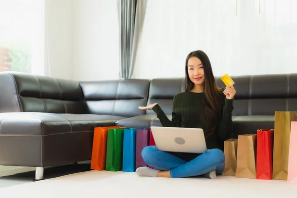 漂亮的年轻亚洲女人在家里用手提电脑和带有购物袋的信用卡进行网上购物 — 图库照片