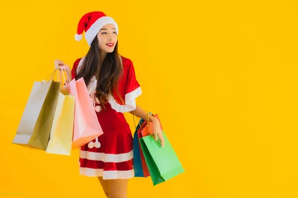 肖像画美しい若いアジアの女性は 黄色の隔離された背景に買い物袋の多くとクリスマス服の帽子を着用 — ストック写真