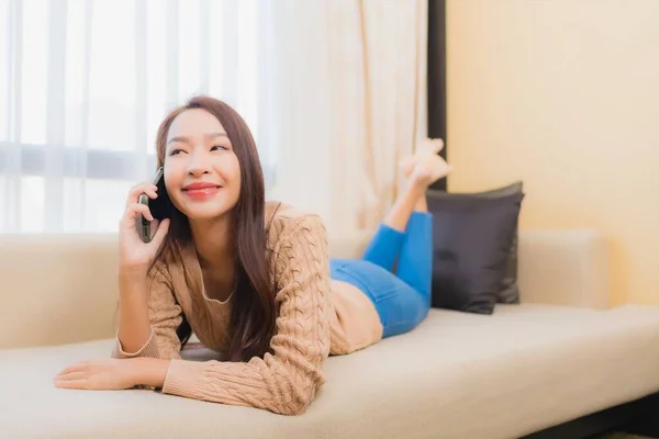 美丽的年轻亚洲女人 用智能手机和咖啡坐在沙发上 开心地放松笑容 — 图库照片