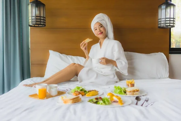 照片中年轻的亚洲女人躺在床上 在卧室里吃早餐 — 图库照片
