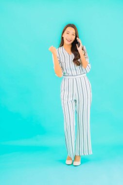 Güzel bir Asyalı kadın portresi mavi arka planda akıllı cep telefonu kullanıyor.