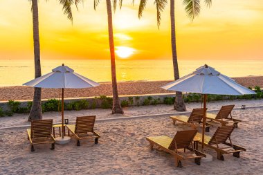 Şemsiye ve güverte sandalyesi günbatımında tropikal deniz okyanusunda ya da gün doğumunda boş zaman ve tatil için