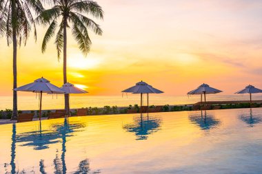 Şemsiye güvertesi sandalyesi oteldeki yüzme havuzunda deniz kıyısı ve gün batımında hindistan cevizi palmiyesi ile birlikte.