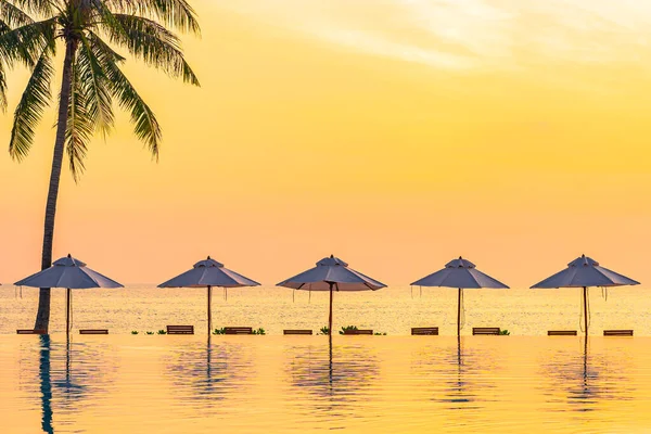 日落或日出时 酒店内设有海滨及椰子树的度假胜地 泳池周围设有伞形甲板座椅 — 图库照片