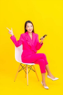 Güzel bir Asyalı kadın portresi sarı renkli izole edilmiş arka planda akıllı cep telefonu kullanır.