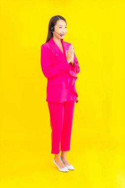 Sarı arka planda çağrı merkezi teması için kulaklığı ve kulaklığı olan güzel Asyalı kadın portresi