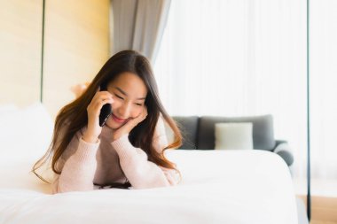 Yatak odasındaki yatağın üstünde kahve fincanı ve cep telefonu olan güzel Asyalı kadın portresi.