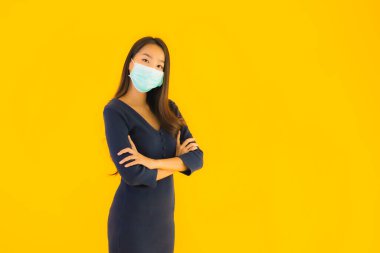 Koronavirüsten korunmak için maske takmış güzel Asyalı bir kadın portresi ve sarı izole edilmiş arka planda 19 numara.