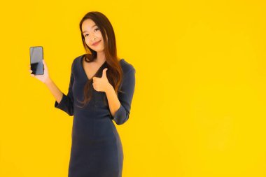 Akıllı cep telefonlu güzel Asyalı kadın portresi ya da sarı izole edilmiş arka planda cep telefonu.