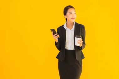 Portre güzel genç Asyalı kadın akıllı cep telefonu ve kahve fincanı ile izole edilmiş sarı arka planda