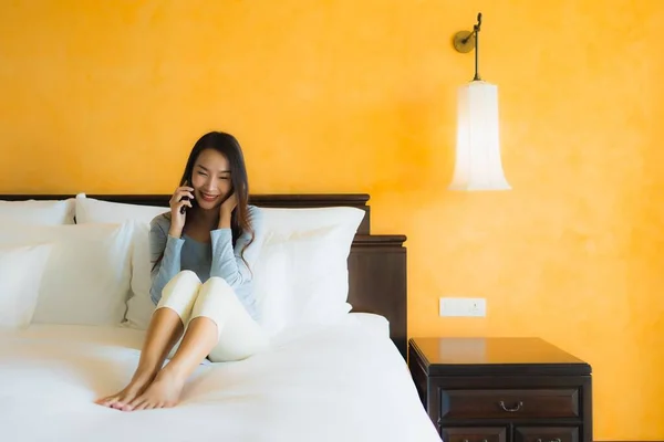 Portrait beautiful young asian woman using mobile cell phone on bed with coffee cup in bedroom interior