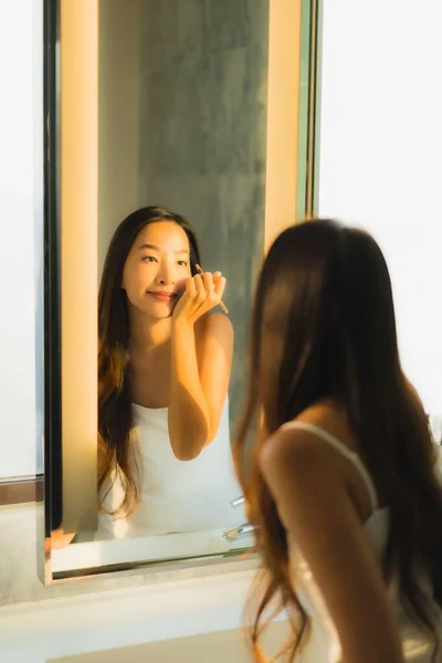 ポートレート美しいです若いですアジアの女性作るとともに化粧品粉末と口紅オン彼女の顔でバスルーム内装 — ストック写真