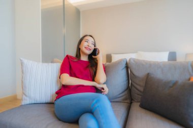 Güzel bir Asyalı kadın portresi. Yatak odasının iç tarafındaki oturma odasındaki koltukta akıllı cep telefonu kullanıyor.