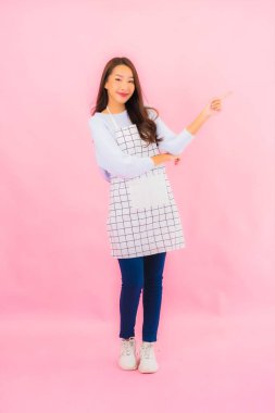 Portrait beautiful young asian woman in kitchen wear with apron on pink isolated background