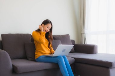 Genç Asyalı bir kadının oturma odasında çalışmak için dizüstü bilgisayar defteri kullanmasının portresi.