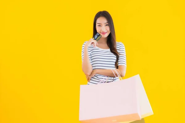 色彩艳丽的年轻亚洲女人 背负着五颜六色的购物袋和黄色独立背景的信用卡 — 图库照片