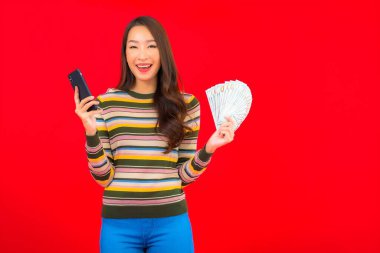 Kırmızı arka planda nakit parası ve cep telefonu olan güzel Asyalı kadın portresi.