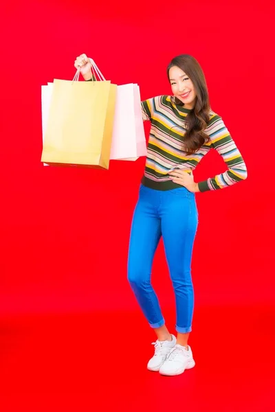 カラフルなショッピングバッグとクレジットカードを持つ肖像画の美しい若いアジアの女性赤の背景 — ストック写真