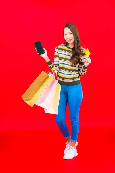 色彩艳丽的年轻亚洲女人 背景是红色的购物袋和信用卡 — 图库照片